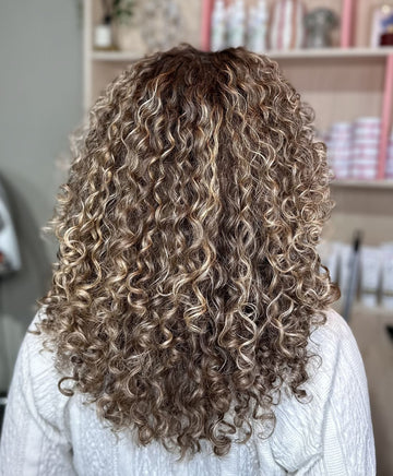 Vrouw met blonde krullen in witte trui