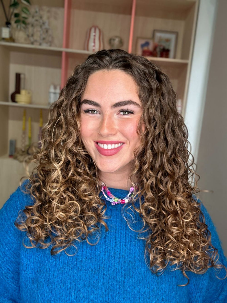 Vrouw met lange krullen glimlacht naar camera